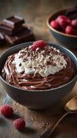 Decadent chocolate mousse topped with whipped cream and fresh raspberries in a cozy setting with chocolate bar pieces photo