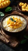 Creamy rice pudding topped with fresh mango cubes and mint leaf on a rustic wooden table photo