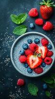 Fresh berries and chia pudding served in a bowl on a dark textured surface with mint leaves garnishing the dish photo