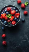 Fresh bowl of mixed berries with mint leaves on dark stone background for healthy eating photo