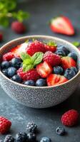 Freshly prepared berry bowl with strawberries, blueberries, and raspberries garnished with mint leaves on a dark background photo
