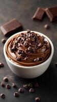 Decadent chocolate frosting in a bowl with chocolate chips on top and chocolate squares nearby photo