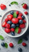 Colorful bowl of chia seed pudding topped with fresh berries and mint on a textured gray surface photo