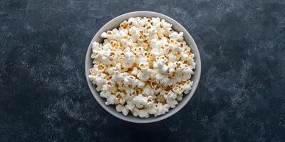 Large bowl filled with freshly popped popcorn sitting on a textured dark surface photo