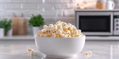 Freshly popped popcorn in a white bowl on a kitchen countertop with modern appliances in the background photo