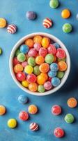 Colorful assortment of gummy candies in a bowl on a blue surface with scattered sweets around photo