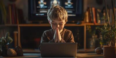 Young child prays quietly at a laptop in a cozy room during evening hours photo