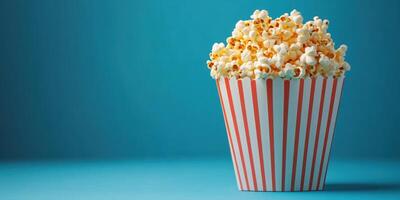 Freshly popped popcorn in a red and white striped container against a blue background photo