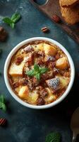 Decadent dessert served in a bowl featuring layers of cake, fruit, and creamy sauce topped with mint leaves and nuts photo