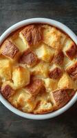 Delicious bread pudding served in a white bowl on a dark background, showcasing golden crust and soft texture photo