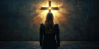 Woman standing in front of illuminated cross in dimly lit room during evening contemplation photo