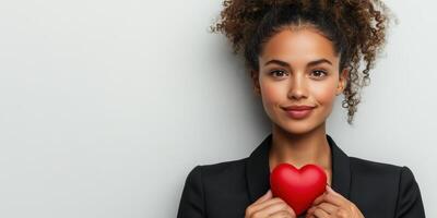 Confident woman smiling while holding a red heart symbol in a professional setting photo