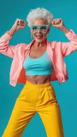 Joyful elderly woman in vibrant outfit celebrating with raised fists against turquoise backdrop photo
