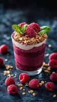 Delicious raspberry parfait topped with granola and mint leaves on a dark textured background photo