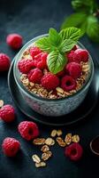 Fresh raspberry parfait with granola and mint leaves served in a glass bowl on a dark background photo