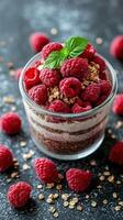 Raspberry parfait with granola and yogurt topped with fresh berries on a dark textured background photo