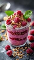 Vibrant raspberry parfait with granola in a glass jar on a textured surface photo