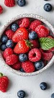 Fresh assortment of berries displayed in a ceramic bowl on a textured surface during the day photo