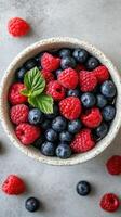 Fresh berries in a rustic bowl on a textured surface with green leaves for a healthy snack or dessert option photo