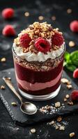 Delicious layered dessert featuring raspberries and crushed nuts served in a glass with whipped cream photo