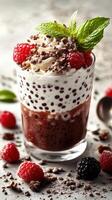 Delicious chocolate dessert topped with cream, raspberries, and mint served in a clear glass on a textured surface photo