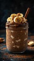 Creamy banana chocolate smoothie topped with sliced bananas and nuts in a jar on a dark background photo