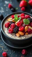 Fresh mixed berry bowl topped with almonds and mint on a dark surface photo