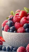 Freshly picked raspberries and blueberries in a textured bowl on a clean table setting in natural light photo