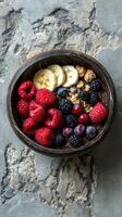Healthy breakfast bowl filled with mixed berries, banana slices, and granola on textured stone surface photo