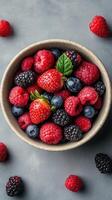 Fresh assorted berries in a bowl placed on a grey surface showcasing vibrant colors and textures photo