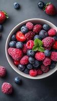 Fresh berry mix featuring strawberries, blueberries, raspberries, and blackberries arranged in a bowl on a dark surface photo