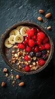 Healthy smoothie bowl topped with bananas, raspberries, blackberries, and nuts served on a black textured surface photo