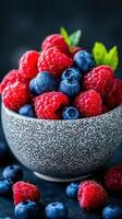 Fresh raspberries and blueberries in speckled bowl on dark background showcasing vibrant summer fruits photo