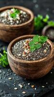 Chia seeds and sesame seeds displayed in wooden bowls with fresh mint leaves on a dark countertop photo