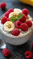 Delicious bowl of yogurt topped with bananas, raspberries, and chia seeds on a dark surface photo