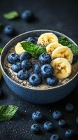 Delicious smoothie bowl topped with blueberries, banana slices, and mint leaves on a dark background photo