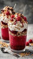 Delicious layered dessert featuring raspberry, granola, and cream served in a glass cup on a textured background photo