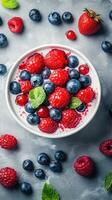 Fresh berries and mint leaves in a white bowl on a textured gray surface photo