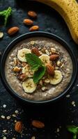 Delicious bowl of oatmeal topped with banana slices, almonds, and mint leaves on a dark background photo