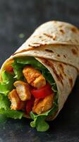 Delicious grilled chicken wrap with fresh lettuce and tomato prepared on a dark surface photo