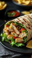 Delicious chicken wrap filled with fresh vegetables and served with chips on a black plate during lunch time photo