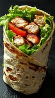 Fresh chicken wrap loaded with lettuce and tomatoes on a dark background ready to enjoy photo