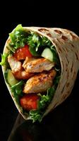 Delicious grilled chicken wrap filled with fresh vegetables and greens on a dark background photo