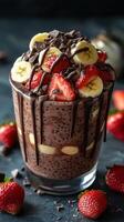 Delicious layered dessert with chocolate, strawberries, and bananas served in a clear glass on a dark background photo
