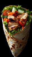 Grilled chicken wrap filled with fresh vegetables served on a black background photo