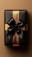 Elegant black gift box with a glossy brown ribbon placed on a neutral background photo