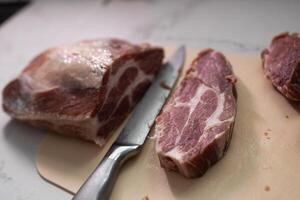 A Freshly Cut Pork Shoulder with a Sharp Knife Resting on the Countertop in the Kitchen photo