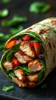 Delicious grilled chicken wrap with fresh vegetables and spinach on a dark background photo