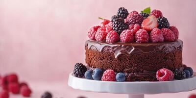 Delicious chocolate cake topped with fresh raspberries, strawberries, blackberries, and blueberries on a white cake stand photo