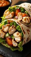 Grilled chicken wraps filled with fresh vegetables, served on a dark stone plate alongside dipping sauce photo